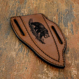 The handcrafted brown leather sheath continues the wilderness theme with a detailed engraving of a bear walking across rugged ground and timber