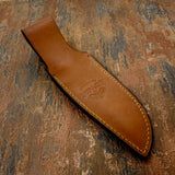 The design is centered along the sheath and framed by reinforced edge stitching, while a snap-retention strap secures the knife firmly in place.
