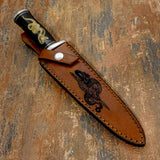 The handcrafted brown leather sheath features a bold engraved composition inspired by ancient symbolism.