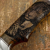 Close-up of a knife handle with a detailed leopard engraving on a textured surface.