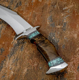 A close-up of a custom fixed-blade knife with a D2 steel blade and a polished handle made of layered brown burl wood and turquoise gemstone inlay