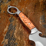 A close-up of a custom knife with a polished silver steel blade and a textured orange Gemstone handle featuring a black crackle pattern