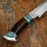 A close-up of a custom knife with a polished silver blade, a dark brown wood handle, and turquoise gemstone inlay details