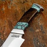 A close-up of a fixed-blade knife with a polished silver blade and a dark brown wood handle featuring turquoise Gemstone inlay