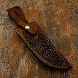 A brown leather knife sheath with an ornate floral tooled design and a silver snap button
