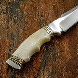 A close-up of  knife with a cream-colored bone handle and gold geometric accents
