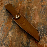 Backside view of A brown leather knife sheath with a partially sheathed knife, featuring silver rivets 