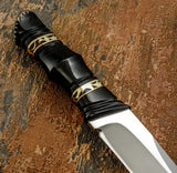 A close-up of a decorative knife with a black bull horn handle individually shaped with sculpted sections featuring brass geometric accents