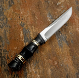 A fixed-blade knife with a polished D2 steel blade and a black handle featuring gold geometric accents, black bull horn with intricate hand-worked contours