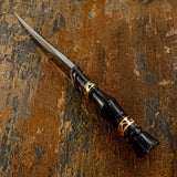 Spine view of A fixed-blade knife with a polished D2 steel blade and a black handle featuring gold geometric accents