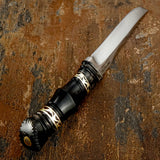 Backside  view of A fixed-blade knife with a polished silver blade and a black Bullhorn handle featuring gold-toned geometric accents
