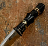 A close-up of a fixed-blade knife with a textured black handle and gold geometric accents, Buy from UK knife store