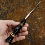 A hand holding a beautiful decorative sleep knife with a slim polished black handle featuring gold geometric accents and a silver blade