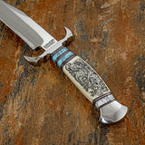Intricate black scrollwork across the camel bone forms the centrepiece of the handle, complemented by carefully arranged gemstone sections, contrasting spacers and sculpted metalwork. The matching scroll-patterned leather sheath completes the presentation.
