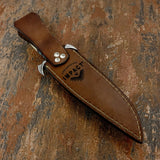 A brown custom leather knife sheath with white stitching and silver metal clips