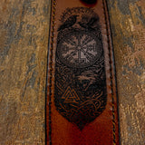 The knife is paired with a handcrafted brown leather sheath featuring deeply engraved Norse-themed artwork.