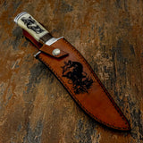 The handcrafted leather sheath displays a dramatic wolf engraving set above a cluster of skulls, creating a bold wilderness motif