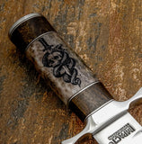 The handle is crafted from deeply engraved camel bone, showcasing a bold skull pierced by a sword while a serpent coils around the blade.
