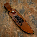 The handcrafted brown leather sheath features a deeply engraved depiction of a wild boar moving across rugged terrain, reinforcing the hunting theme of the knife.